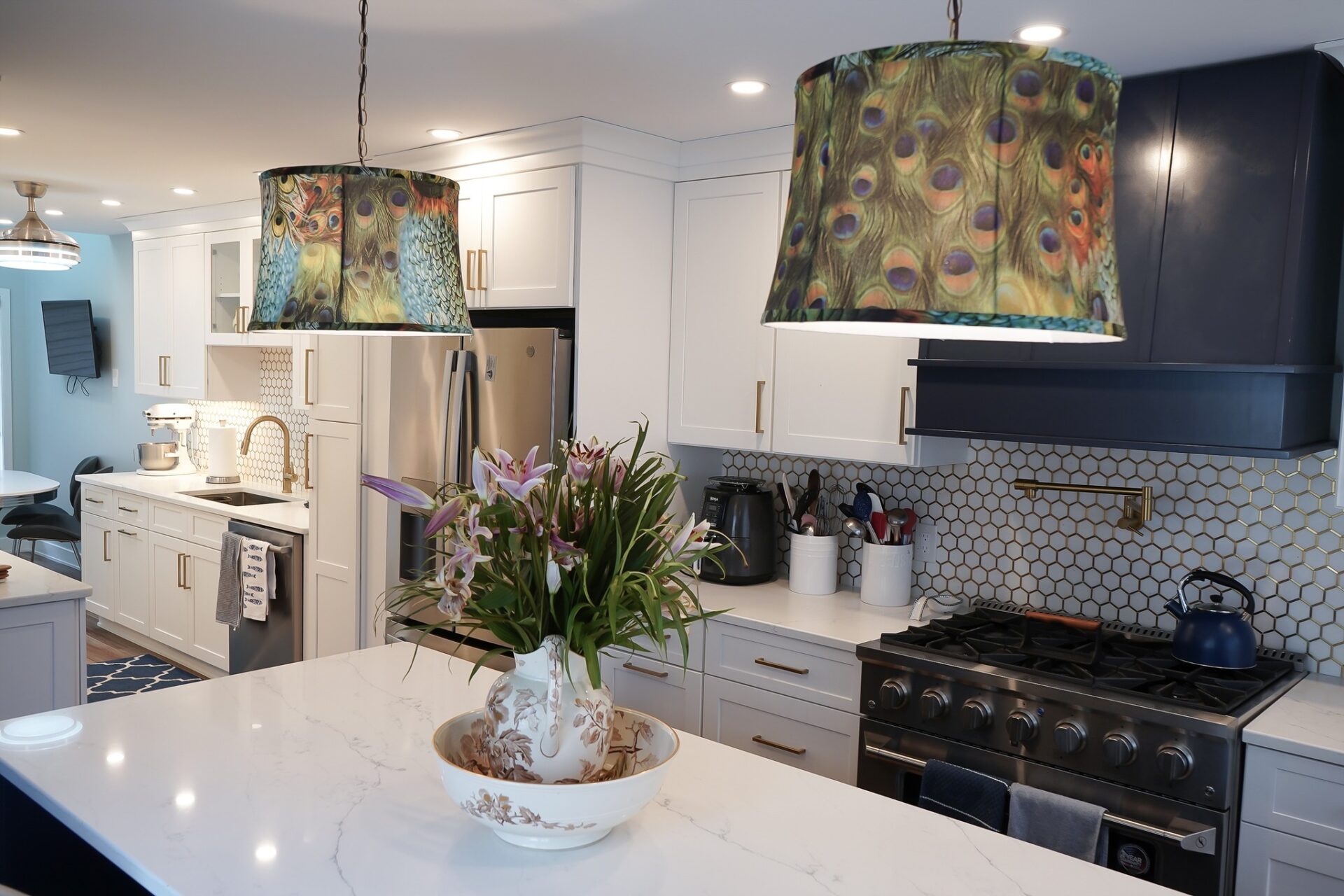 Modern kitchen remodel featuring white shaker cabinets, stainless steel appliances, marble countertops, floral centerpiece, and colorful peacock feather pendant lights — Central Connecticut Building and Remodeling, Berlin, CT.