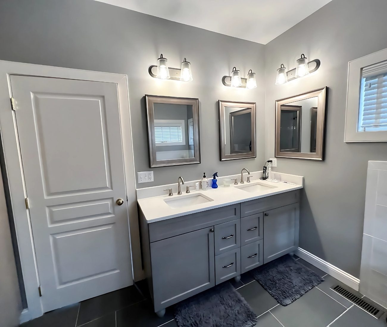 Modern bathroom remodel in Newington CT with double vanity, gray cabinets, framed mirrors, and updated lighting fixtures